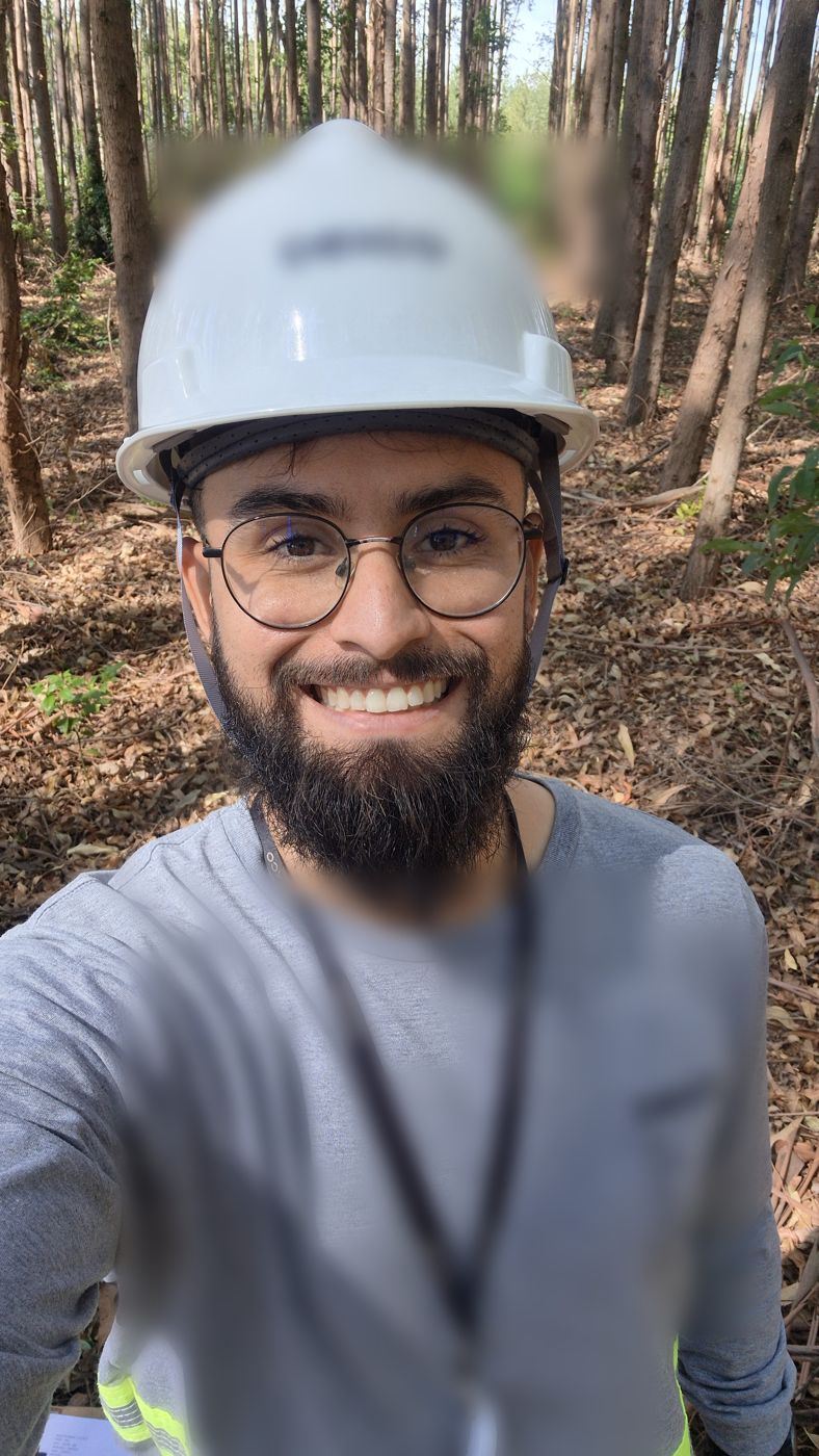 Natan Telles de capacete, sorrindo, em uma floresta de eucalipto
